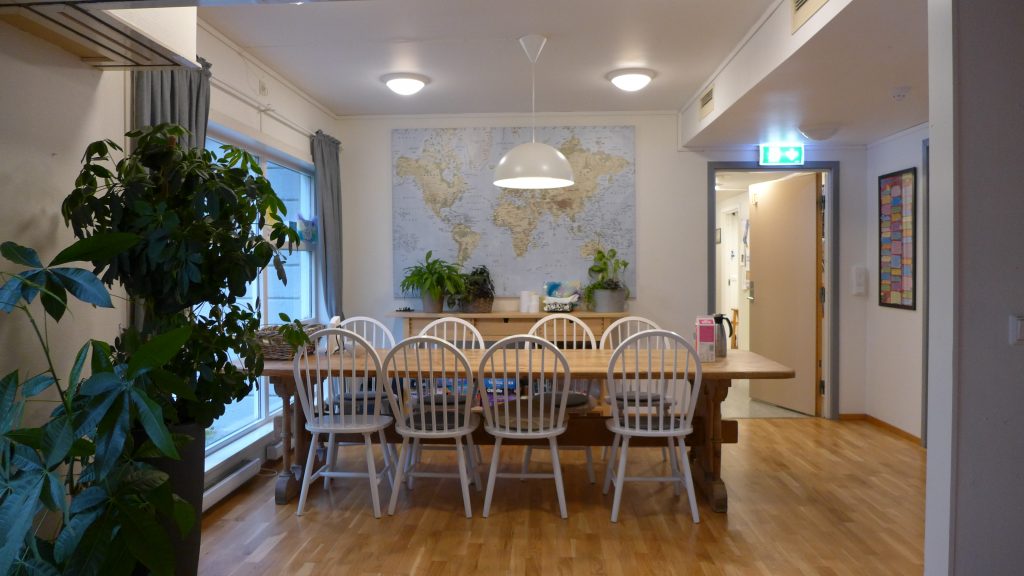 Bord med stoler rundt og potteplante i høyre hjørne