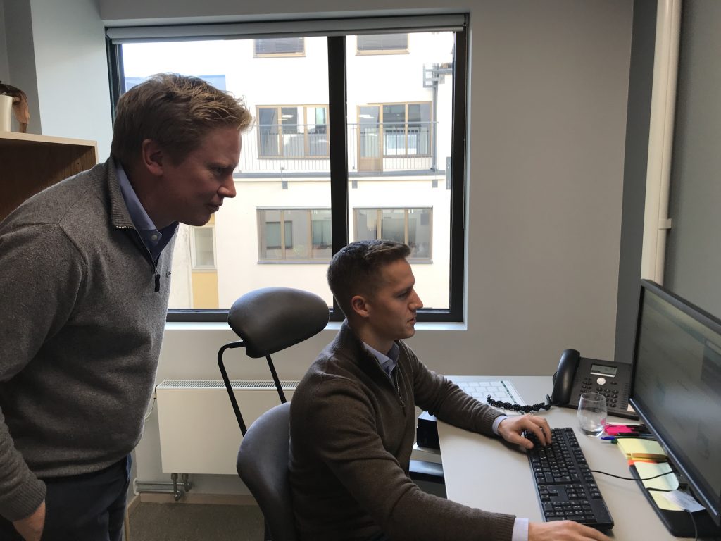 En mann står og ser over skulderen til annen mann som sitter foran PC