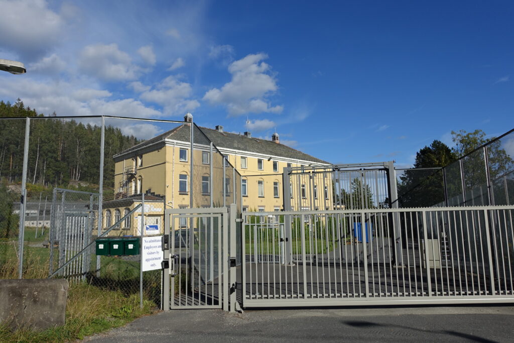 Eksteriørfoto Dikemark - gul bygning bak gjerde med blå himmel over