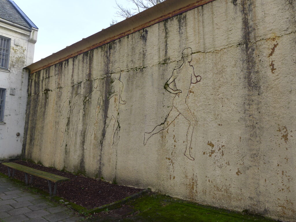 Lys grå murvegg med tegninger av omriss av mennesker som løper