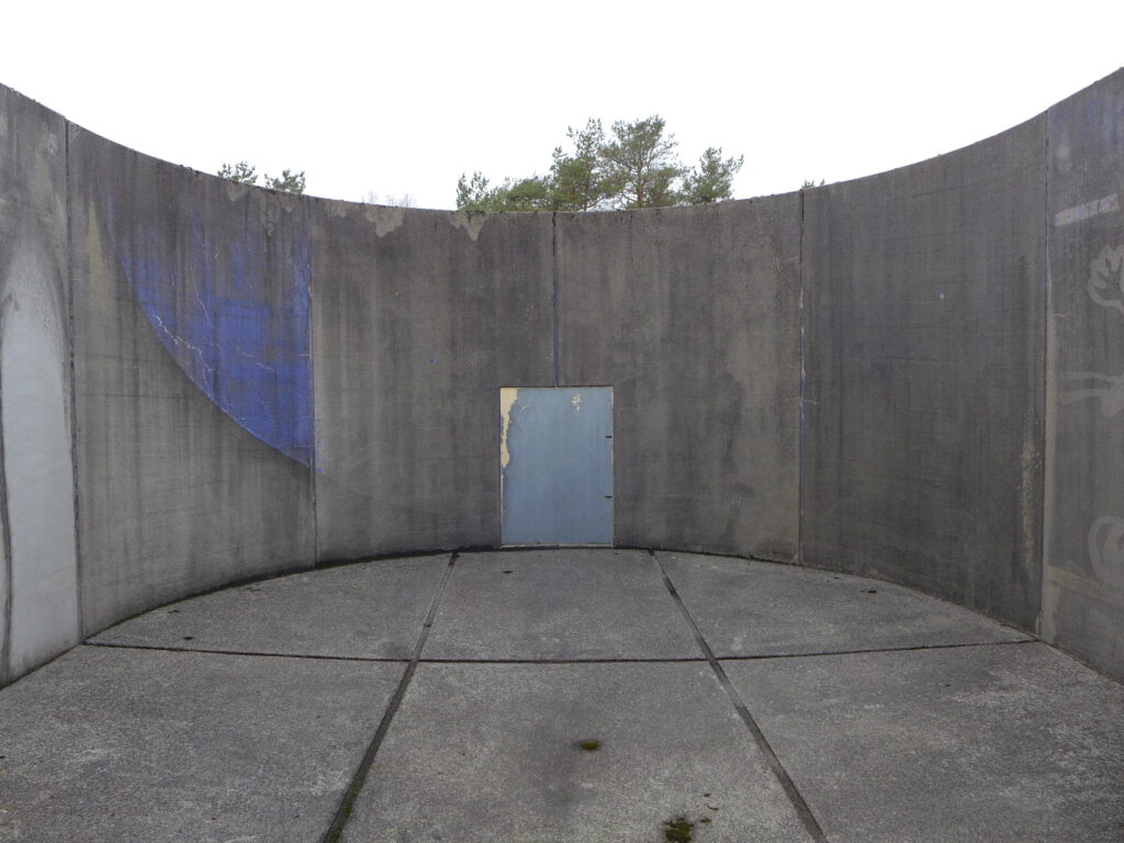 Luftegård i fengsel. Grå murvegger og grått golv, lite glimt av hvit himmel over.