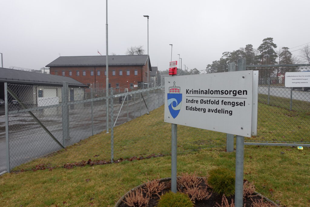 Brunt bygg bak gjerde, skilt foran med teksten 