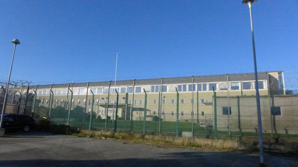 Blå himmel over fengselsbygning bak gjerde.