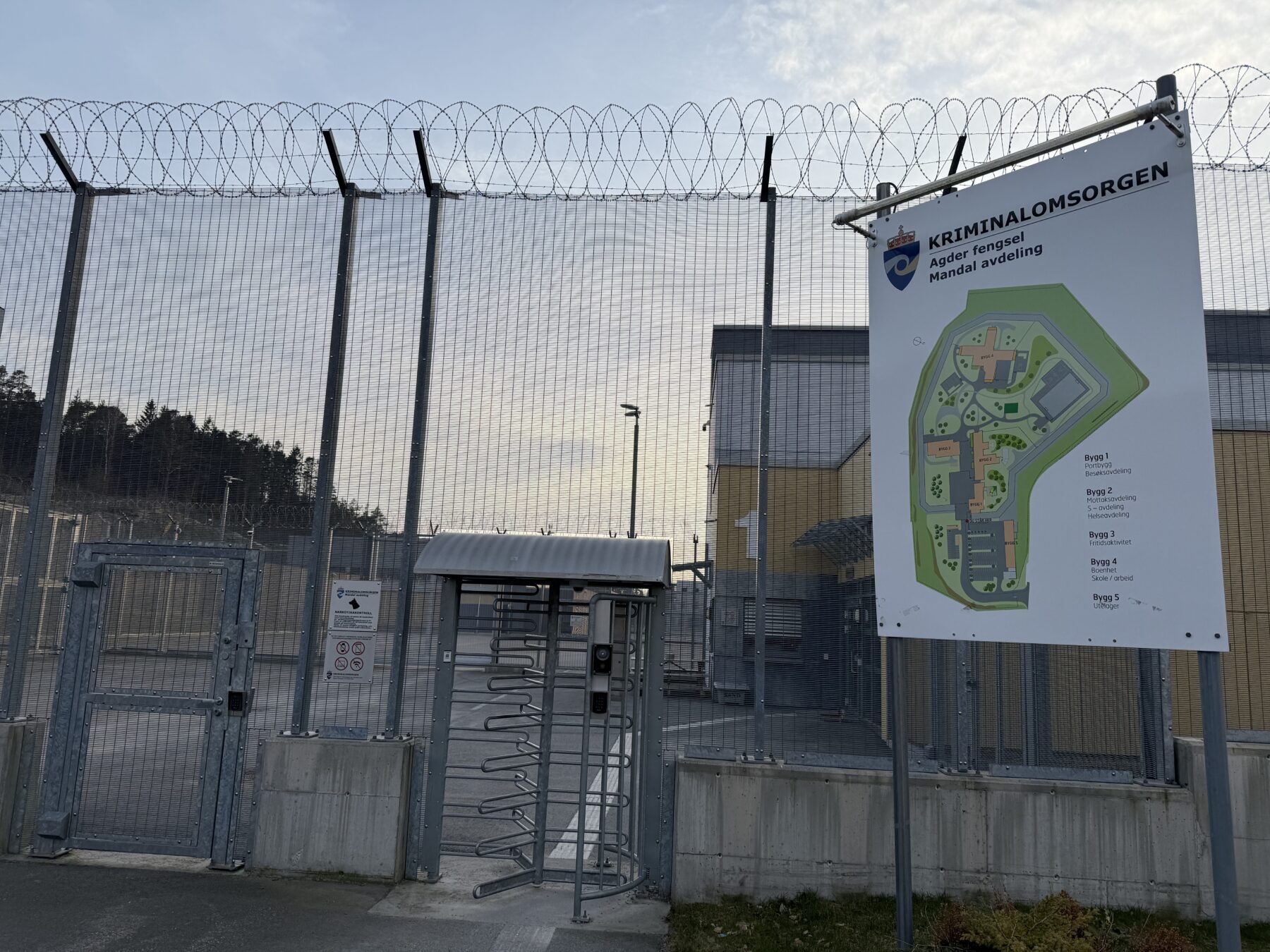 Fengselsbygg bak høye gjerder og med skilt som sier Agder fengsel, Mandal avdeling